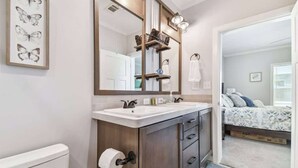 A bathroom with a double sink, a large mirror, and a toilet. There is a towel rack above the mirror and a shelf with toiletries. - 2 Bed Cozy Home, Dade City, Pickle Ball (Dade City)