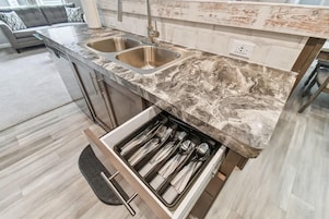 A modern kitchen with two stainless steel sinks, a marble countertop, and a drawer with utensils.