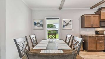 A dining room with a long table, wooden chairs, and a view through a glass door to an outdoor area.