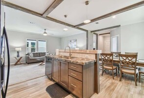 A modern kitchen with wooden cabinets, a marble countertop, and a dining area with wooden chairs.