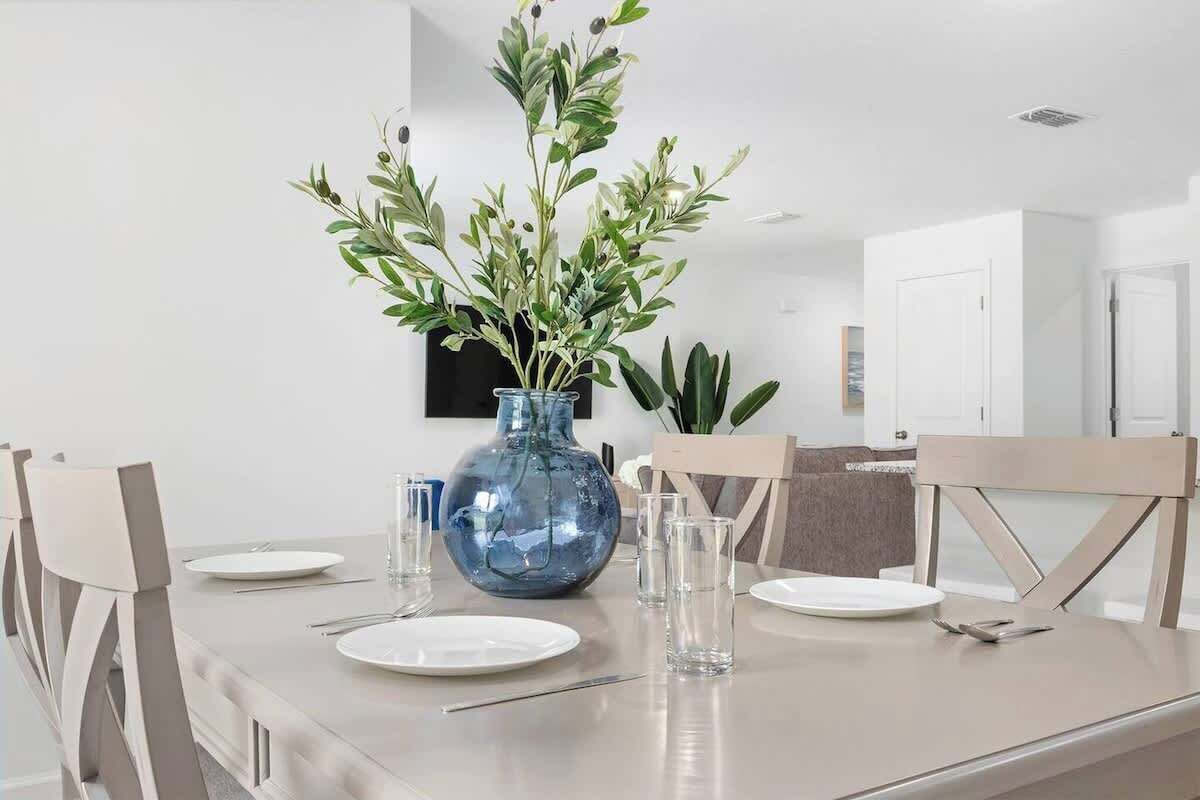 A dining table set with plates, cutlery, and a blue vase with green foliage.