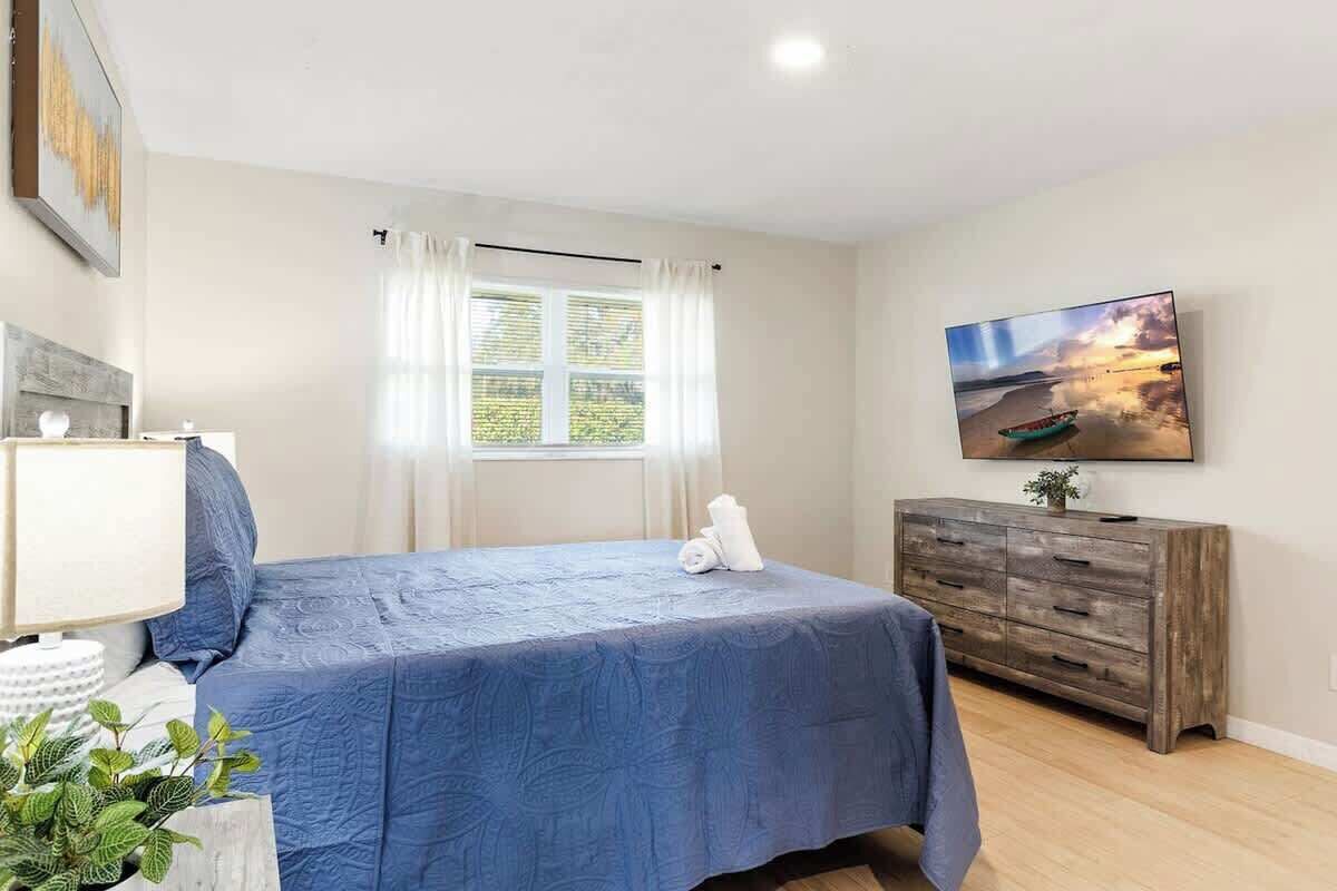 A bedroom with a bed, a dresser, a TV, and a window with curtains.