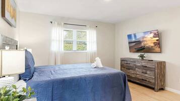 A bedroom with a bed, a dresser, a TV, and a window with curtains.