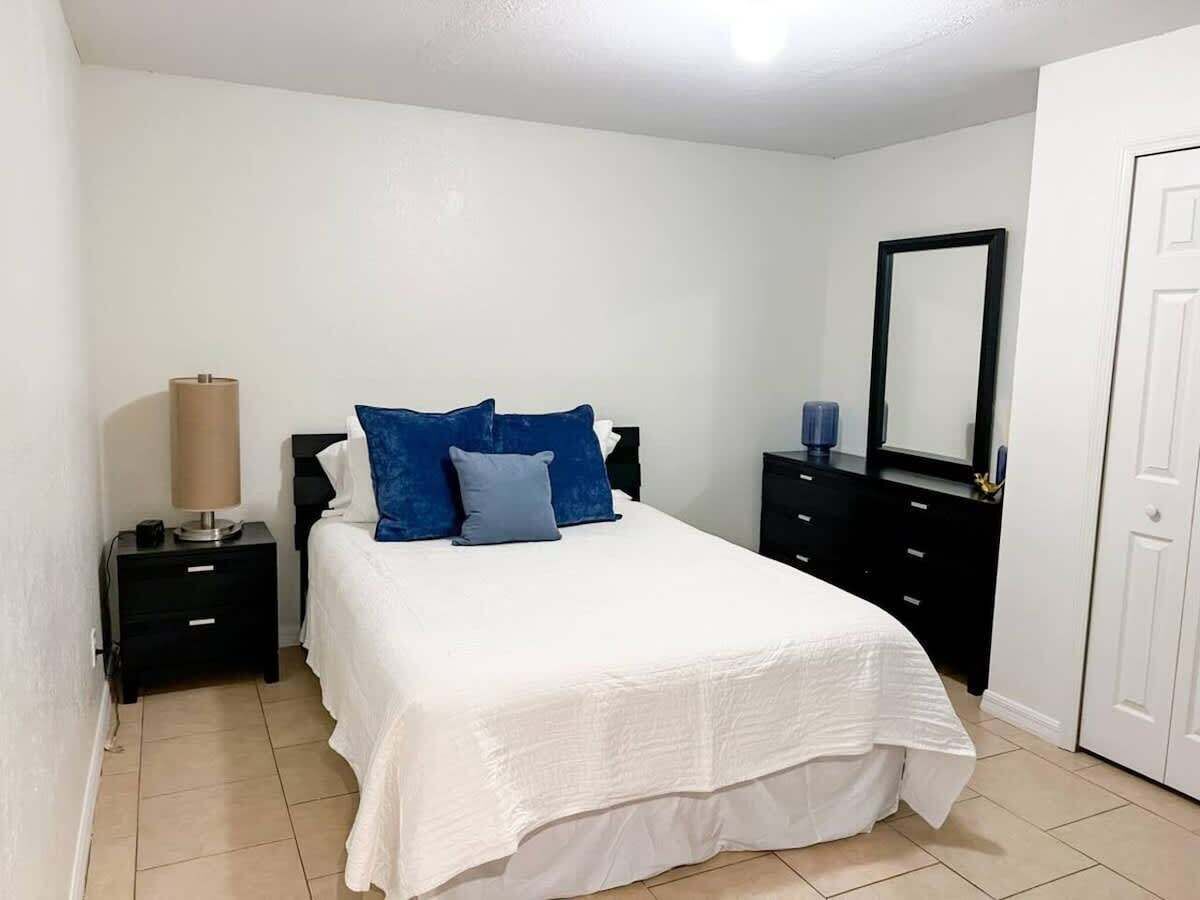 Un dormitorio con cama, mesita de noche, cómoda, espejo y puerta.