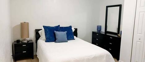 Un dormitorio con cama, mesita de noche, cómoda, espejo y puerta.