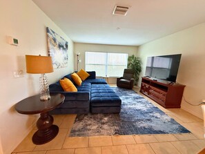 A living room with a sectional sofa, a TV, a lamp, and a painting on the wall.