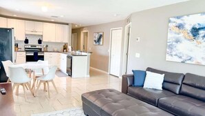 A modern living room with a brown leather sofa, a dining table with chairs, and a kitchen in the background. - Contemporary 3 Bedroom Home in Dade City (Dade City)