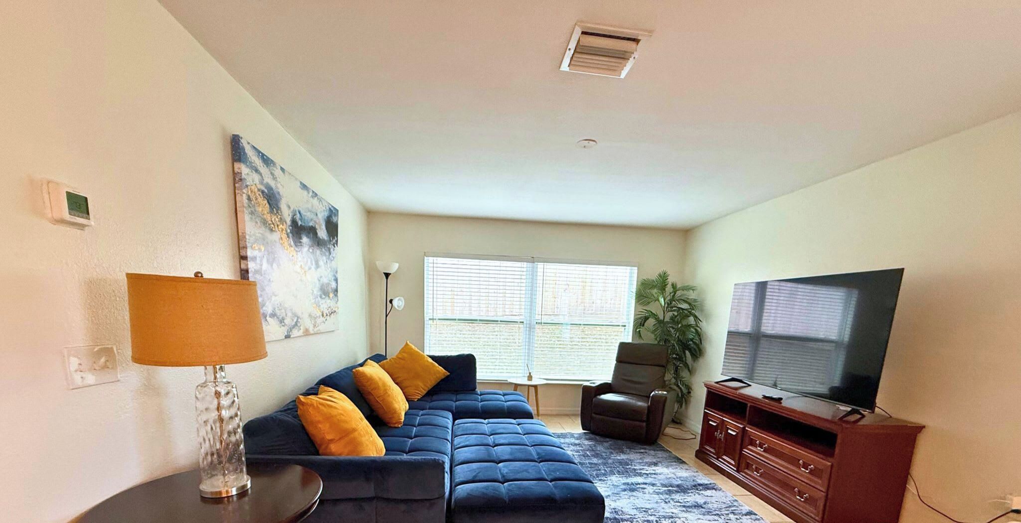 Una sala de estar con un sofá modular, un televisor, una lámpara y una ventana con persianas.