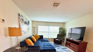 Una sala de estar con un sofá modular, un televisor, una lámpara y una ventana con persianas.