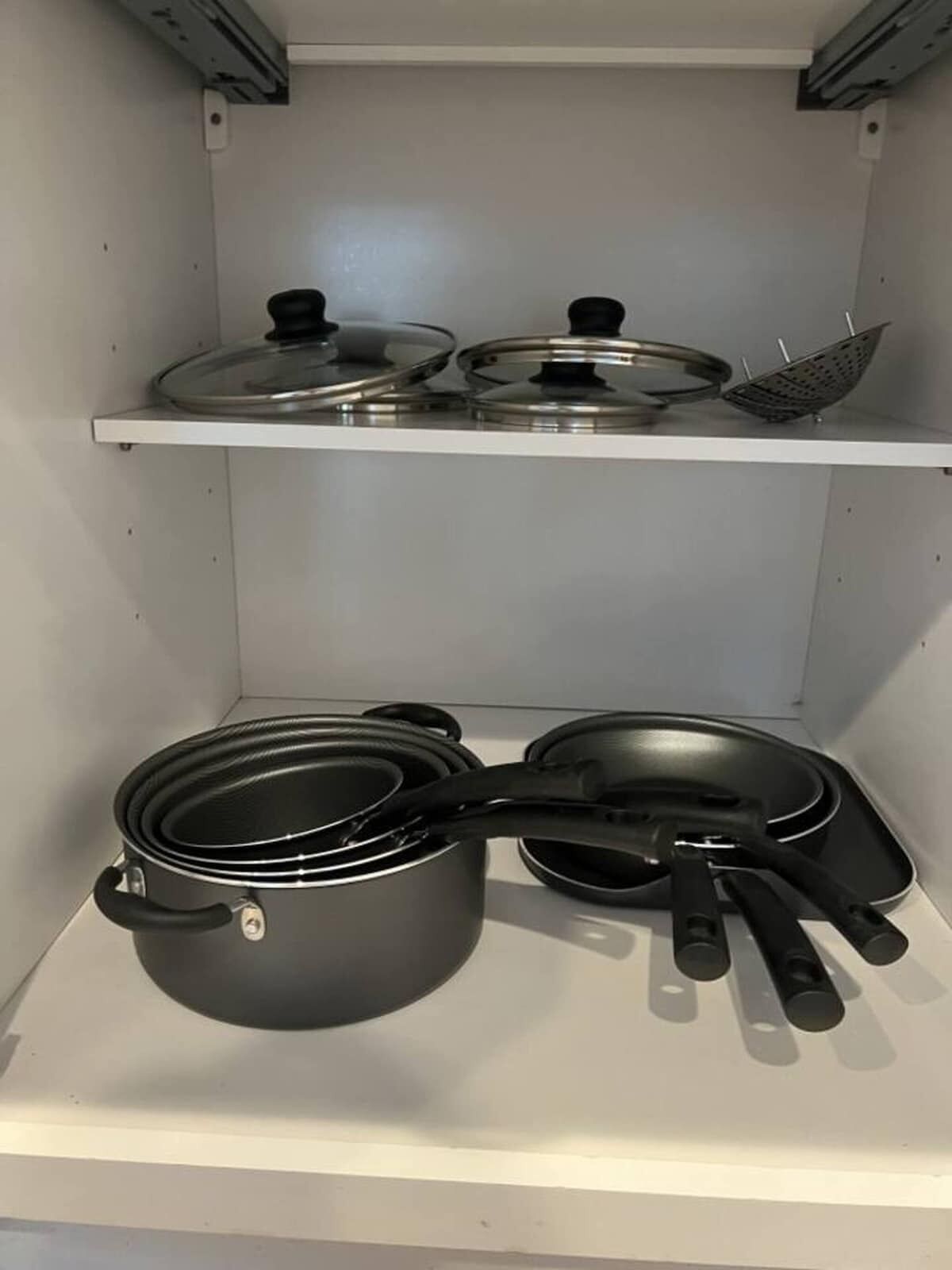 Una cocina con utensilios de acero inoxidable, incluyendo ollas y sartenes, sobre una repisa blanca.