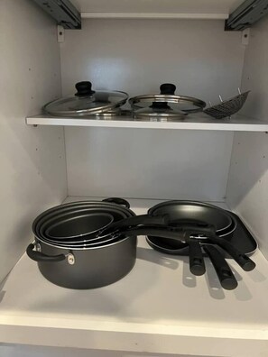 A kitchen with stainless steel cookware, including pots and pans, on a white shelf.