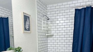 A bathroom with white subway tiles, a white sink with a granite countertop, a white toilet, and a bathtub with a blue shower curtain. - Contemporary 3 Bedroom Home in Dade City (Dade City)
