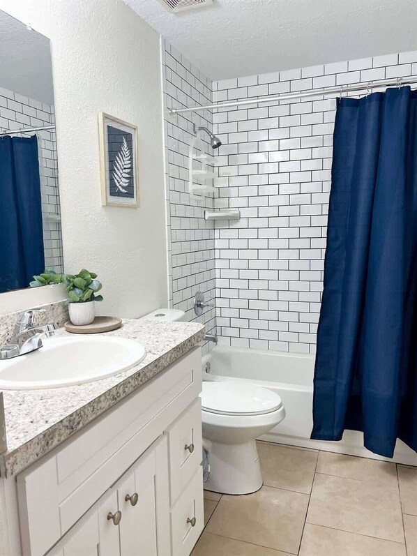 A bathroom with white subway tiles, a white sink with a granite countertop, a white toilet, and a bathtub with a blue shower curtain.