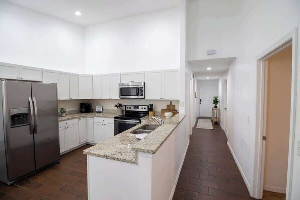 A modern kitchen with white cabinets, stainless steel appliances, and a granite countertop. - Entire Modern Home in Dade City (Dade City)