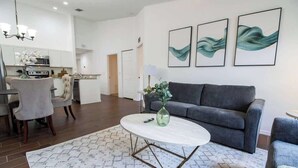 A modern living room with a grey sofa, a round coffee table, and a patterned rug. There is a dining area with a white table and chairs, and a kitchen in the background. - Entire Modern Home in Dade City (Dade City)