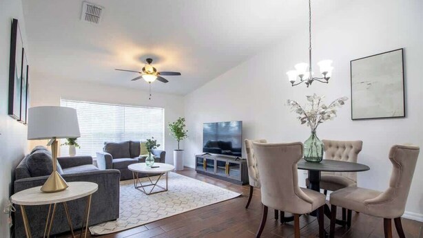 A spacious living room with a ceiling fan, a dining area with a chandelier, and a television in the background. - Entire Modern Home in Dade City (Dade City)