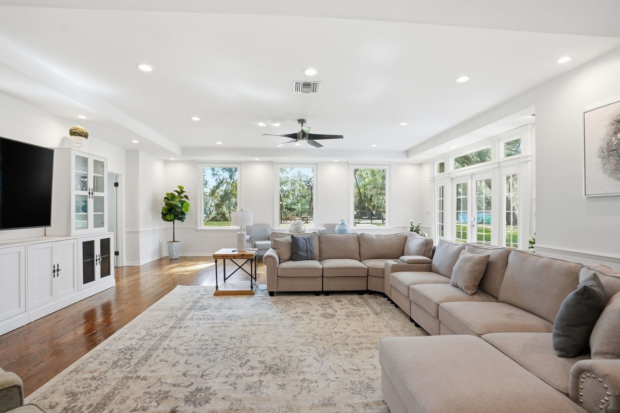 A spacious living room with a large sectional sofa, a flat-screen TV, and a ceiling fan.