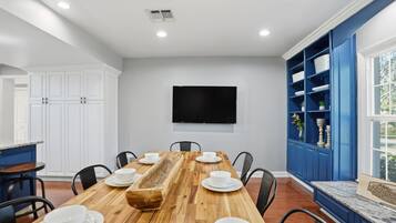A dining area with a wooden table set for six, white chairs, a blue cabinet with decorative items, and a flat-screen TV mounted on the wall.