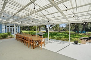 Un patio cubierto al aire libre con una mesa y sillas de madera, una parrilla y vistas a un parque con árboles y una masa de agua.
