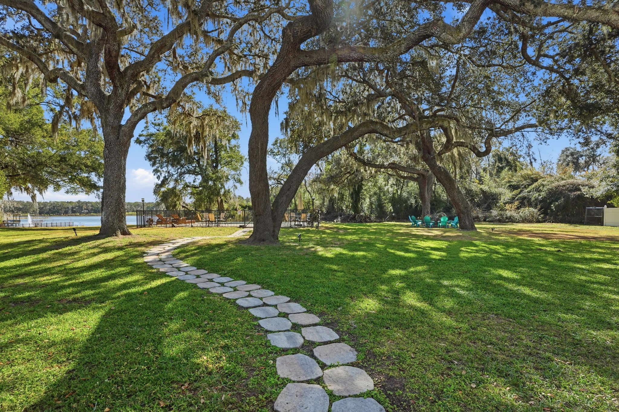 A stone pathway leading through a park with large trees and a lake in the background.