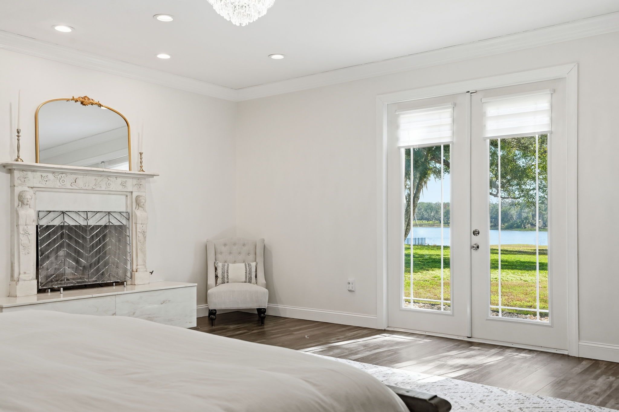 A bedroom with a large bed, a fireplace, a chair, and a view of a lake through glass doors.
