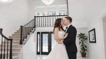 Una pareja se abraza en un vestíbulo amplio y luminoso, con una escalera imponente y un candelabro.