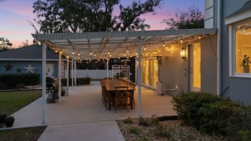 A covered patio with a dining table and chairs, string lights, and a grill.