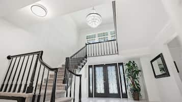A spacious foyer with a grand staircase, a chandelier, and a large potted plant.