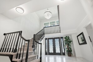 A spacious foyer with a grand staircase, a chandelier, and a large potted plant. - Executive 5 Bedroom Pool Home, Dade City! (Dade City)