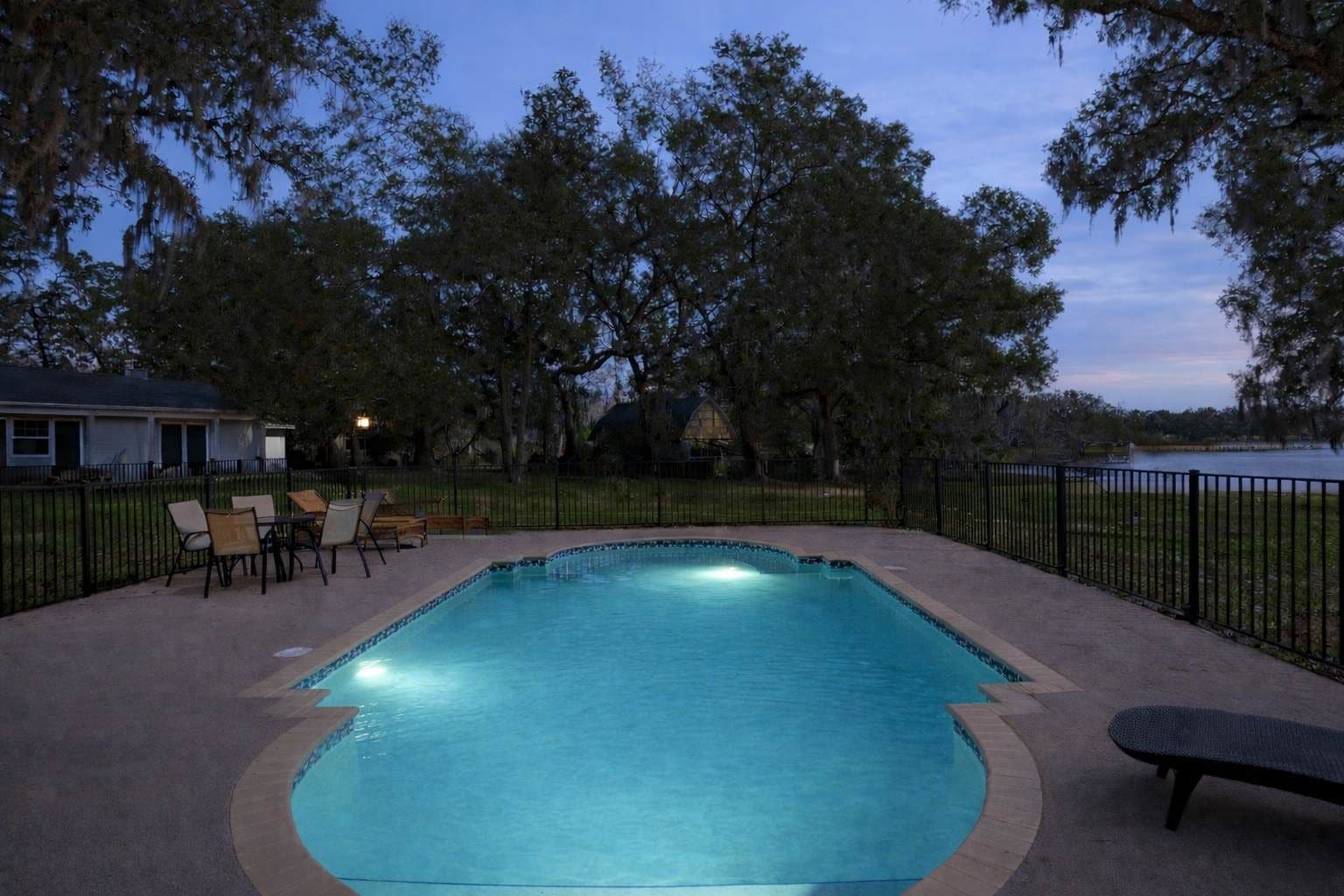 A rectangular swimming pool with a tiled edge, surrounded by a paved deck. There are lounge chairs and a bench around the pool.