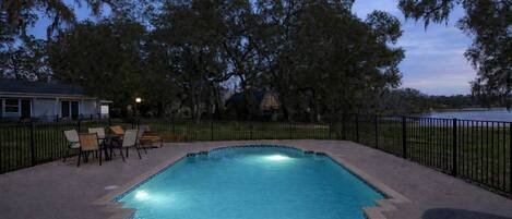 A rectangular swimming pool with a tiled edge, surrounded by a paved deck. There are lounge chairs and a bench around the pool.