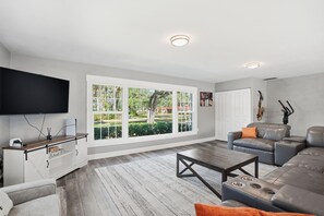 A modern living room with a large window, a flat-screen TV, a leather sofa, and a coffee table. - Executive 5 Bedroom Pool Home, Dade City! (Dade City)