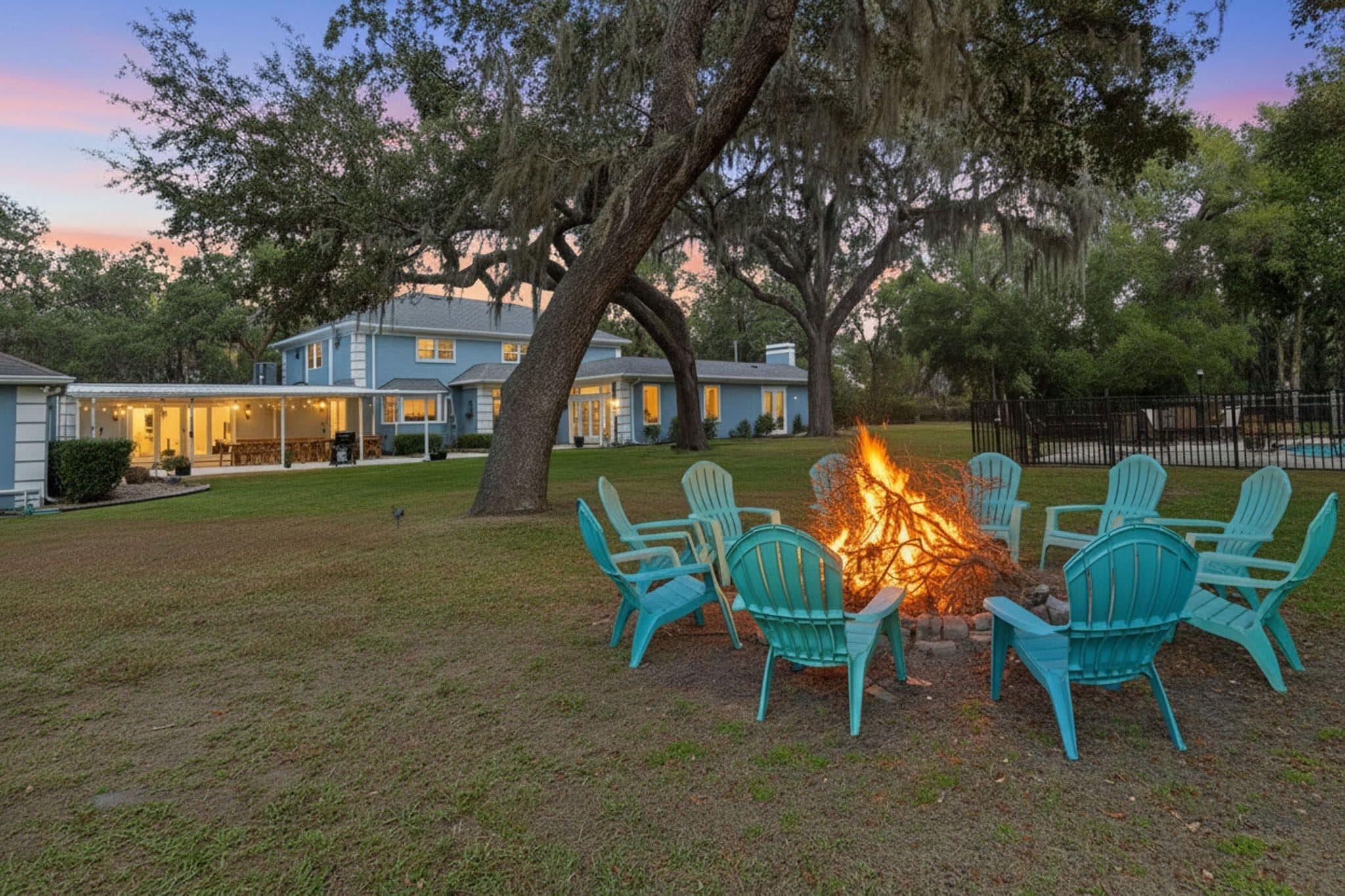 A house with a fire pit surrounded by chairs in a yard.
