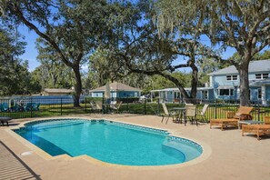 A swimming pool with a curved edge, surrounded by a sandy deck, wicker chairs, and a fence. - Executive 5 Bedroom Pool Home, Dade City! (Dade City)