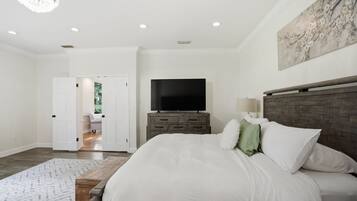 A bedroom with a large bed, a TV on a wooden dresser, and a chandelier.