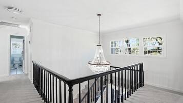 A spacious, well-lit interior with a grand chandelier, a staircase with black railings, and a view through large windows.