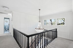A spacious, well-lit interior with a grand chandelier, a staircase with black railings, and a view through large windows. - Executive 5 Bedroom Pool Home, Dade City! (Dade City)