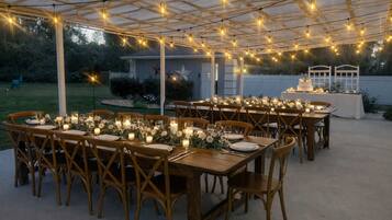 An outdoor dining area with wooden tables and chairs, string lights, and candles.
