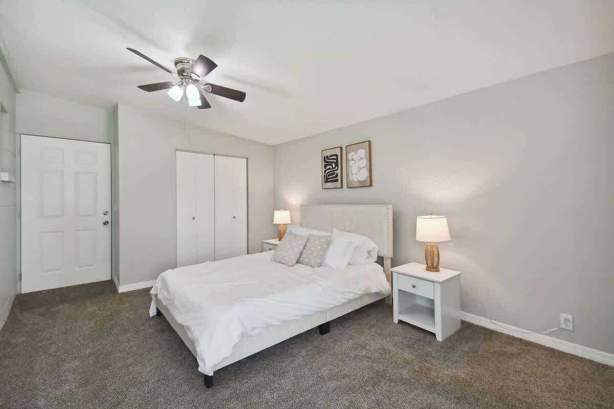 A bedroom with a bed, nightstands, a ceiling fan, and a door.