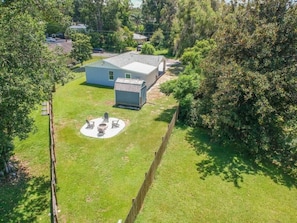 Ein Haus mit eingezäuntem Garten, einer runden Terrasse mit Gartenmöbeln und einem kleinen Gartenhaus.