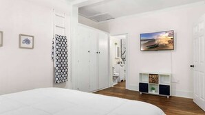 A bedroom with a large bed, a wardrobe, a bathroom visible through an open door, and a painting on the wall. - Charming 1-bedroom Home in Lakeland! (Lakeland)