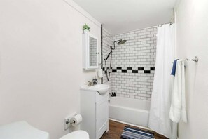 Une salle de bain avec un lavabo blanc, des toilettes et un espace douche, le tout agrémenté d’un mur à carreaux noirs et blancs.