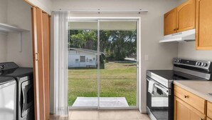 Une cuisine avec une porte-fenêtre coulissante donnant sur un jardin, un lave-linge et une cuisinière.