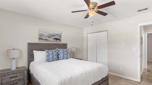 Une chambre à coucher avec un lit, des tables de chevet, un ventilateur de plafond, une porte et un tableau au mur.