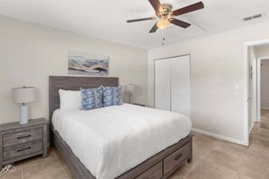 A bedroom with a bed, nightstands, a ceiling fan, a door, and a painting on the wall. - Cozy 2 Bedroom Home, Dade City! #1 (Dade City)