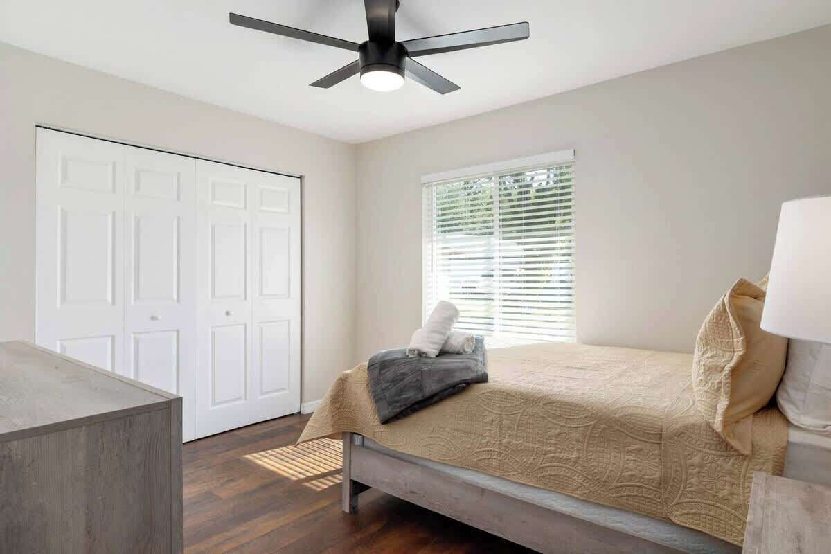 Un dormitorio con cama, ventilador de techo, ventana con persianas y una puerta.