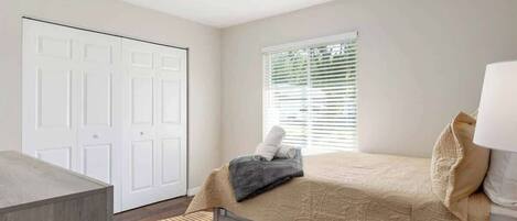 Un dormitorio con cama, ventilador de techo, ventana con persianas y una puerta.