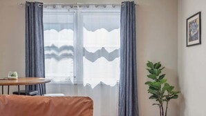 A room with a sofa, a small table with a cup, a potted plant, and a window with curtains. - Historical Art Deco Central Downtown - Sleeps 4 (Anchorage)