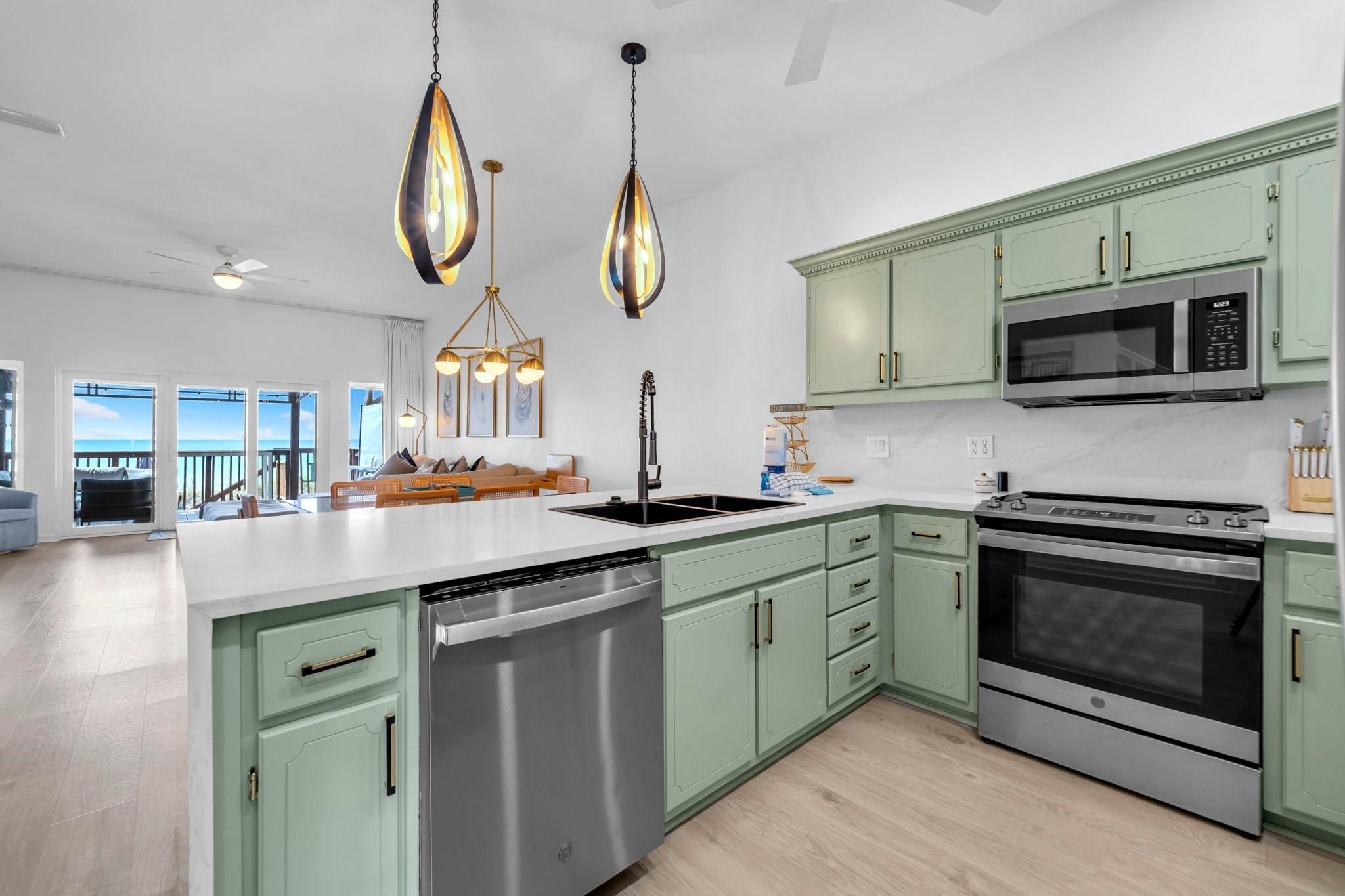A modern kitchen with green cabinetry, stainless steel appliances, and pendant lighting.