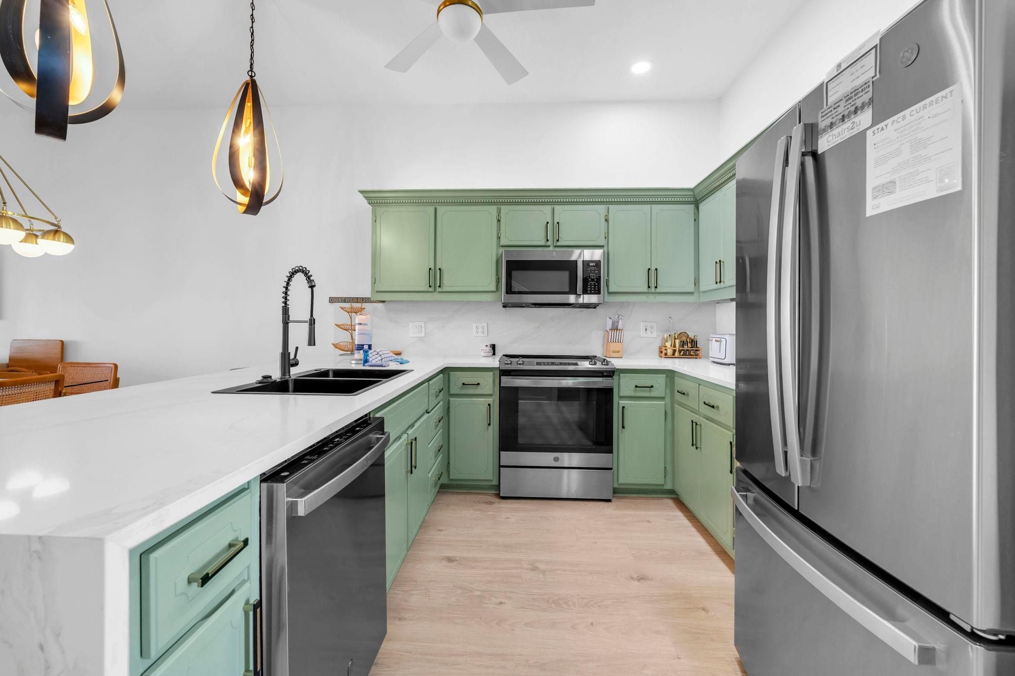 A modern kitchen with green cabinets, stainless steel appliances, a microwave, oven, and a refrigerator.